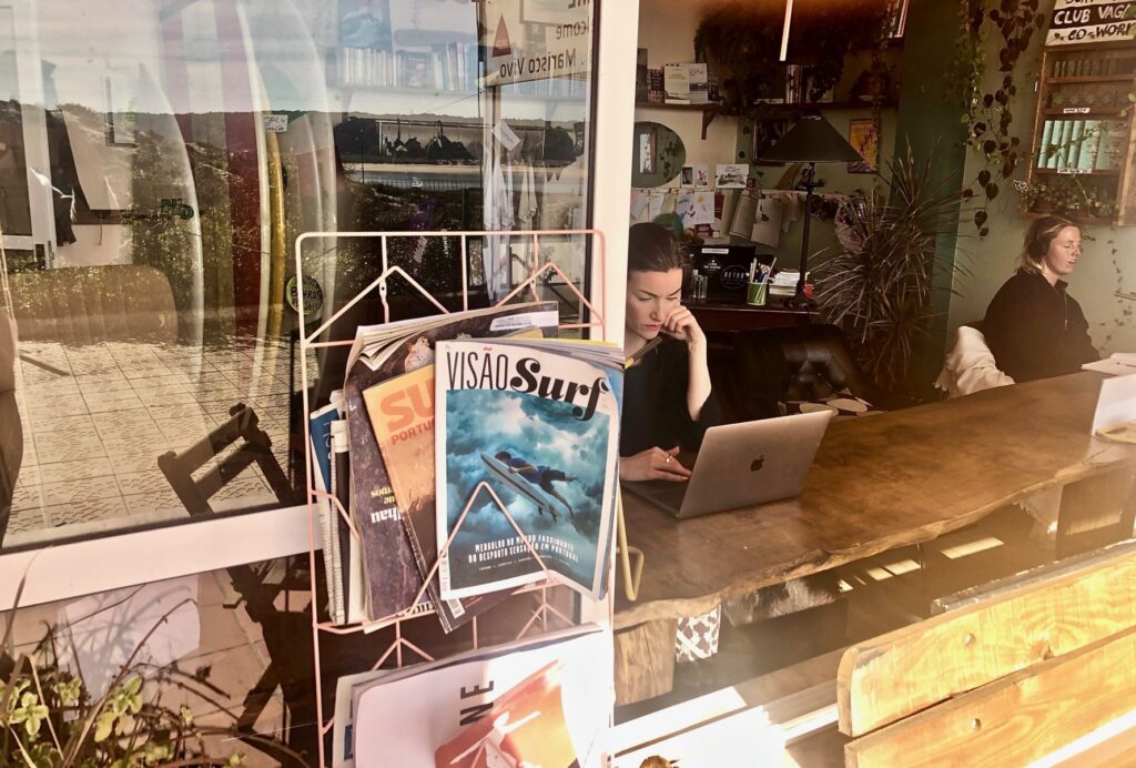 View from outside into the coworking boutique showing a coworker sitting at a desk by the window, focused on her laptop.