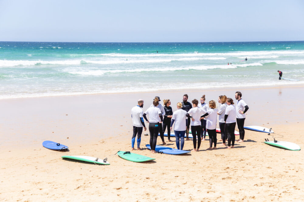 Group of students standing in a circle, attentively listening to instructions, ready to begin their intermediate surf lesson.