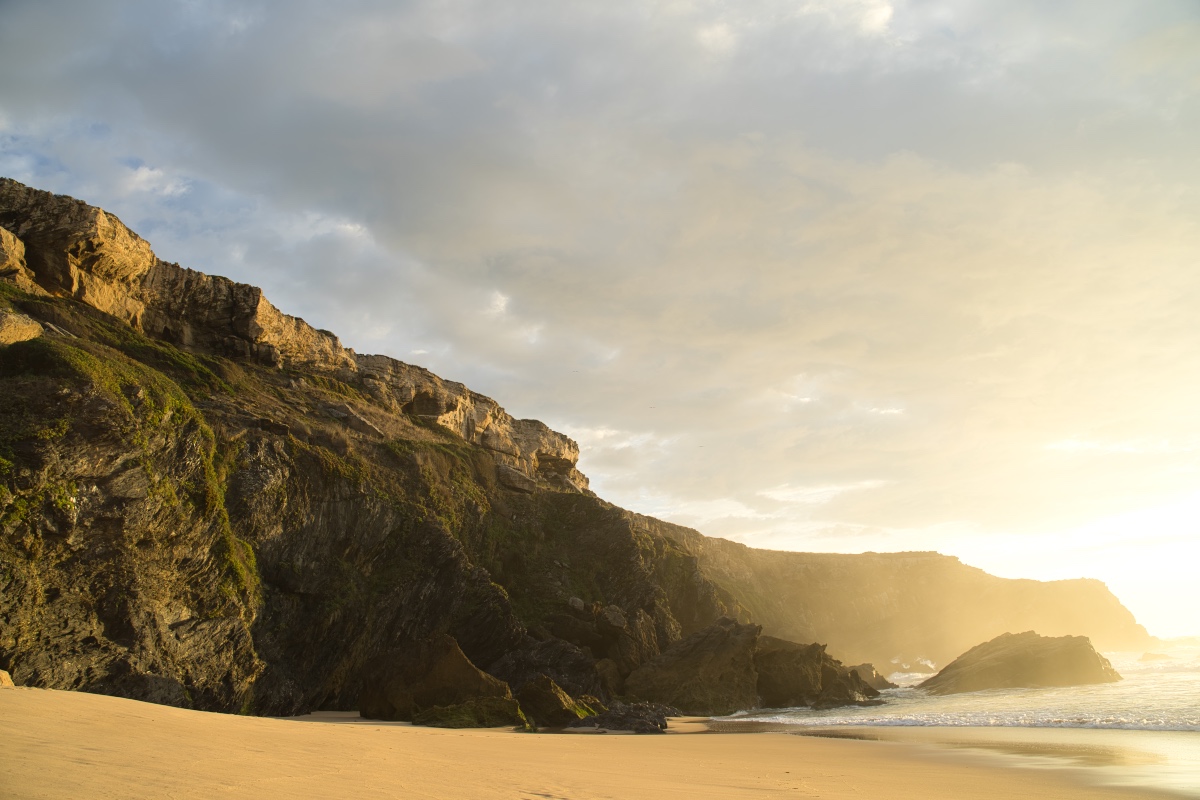 Scenic view of a beach at sunset with soft, warm light and a few scattered clouds in the sky.