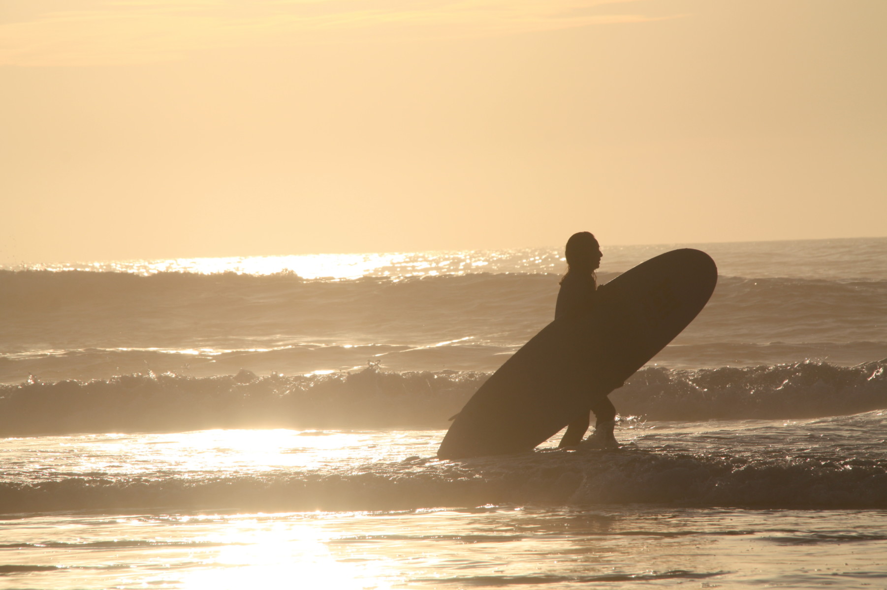 Surf student holding his board, walking out of the water after finishing his intermediate surf lesson.