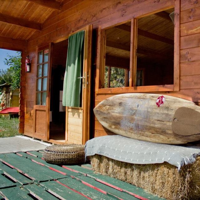 One of the wooden bungalows at Ecosurfcamp, featuring a wooden terrace and large windows, set in a lush garden near Vila Nova de Milfontes.