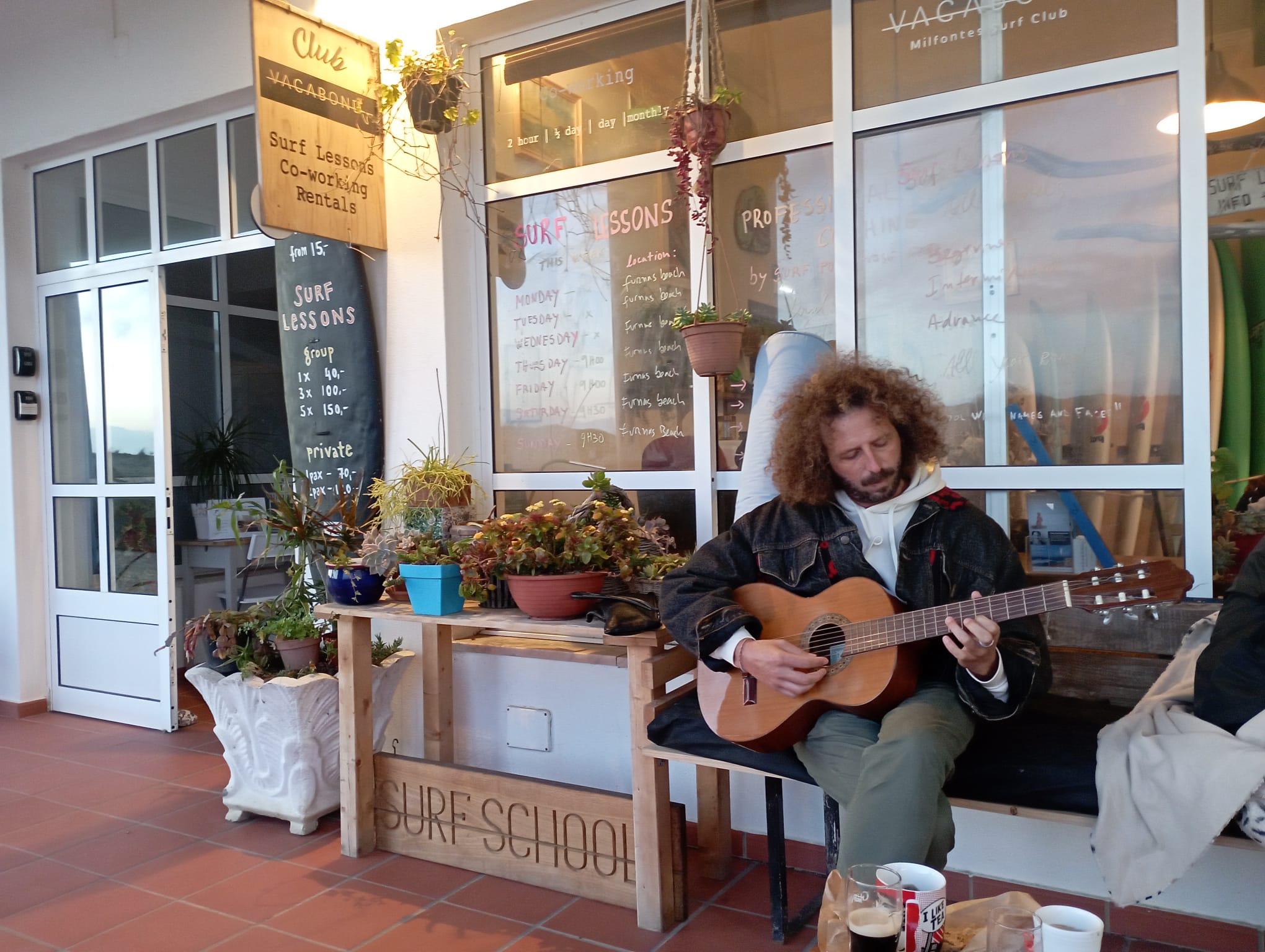 A member of Club Vagabond sitting in front of the surf shop, playing guitar